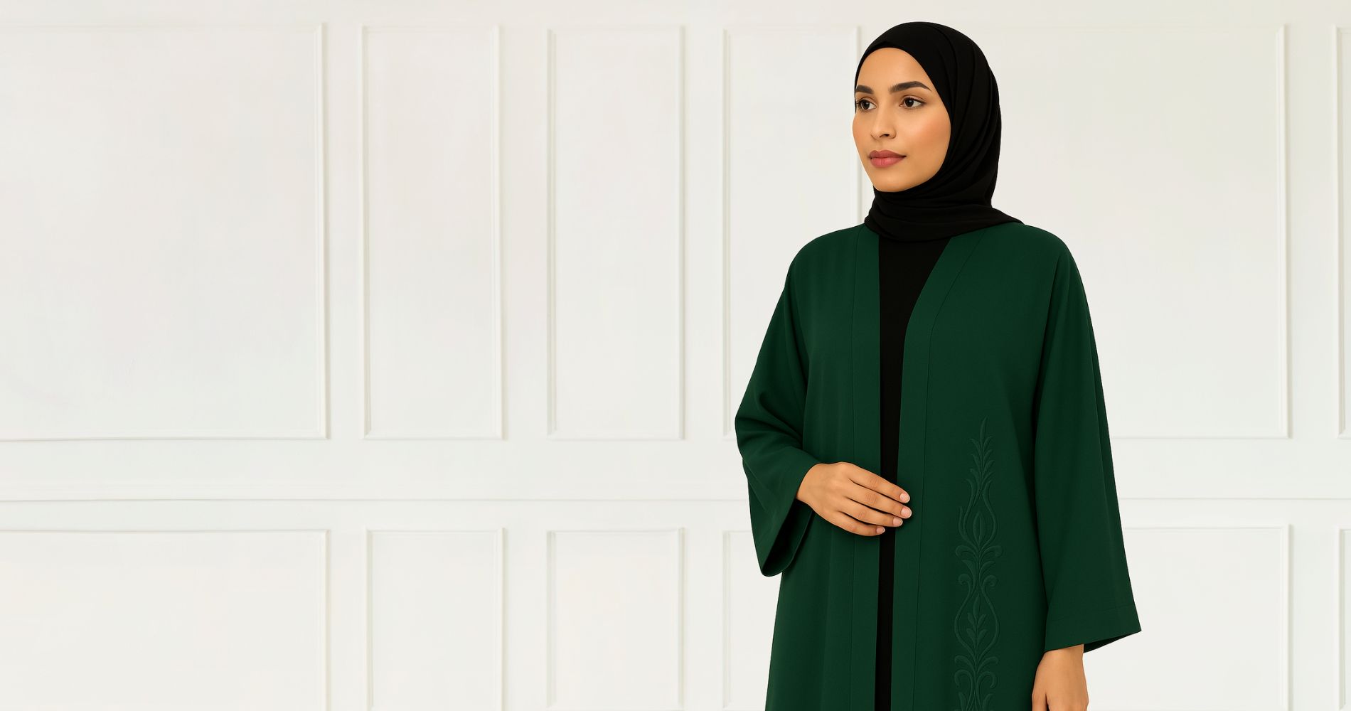 Zanattire dark green embroidered abaya worn by a model in black hijab, posed against a white panel background